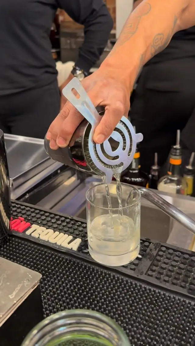 Bartender straining a cocktail into a glass