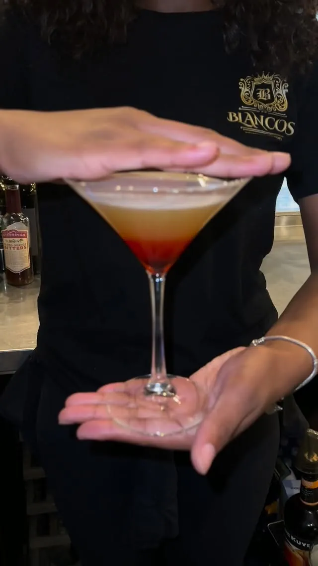 A layered cocktail being presented by a bartender